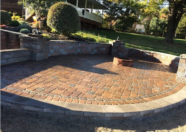 Curved brick patio with stone walls in a residential backyard with green lawn and trees